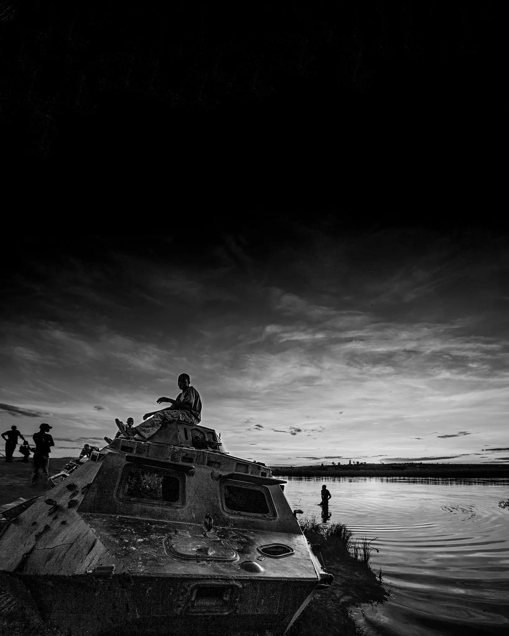 Black and white image of a boy sitting on top of a tank