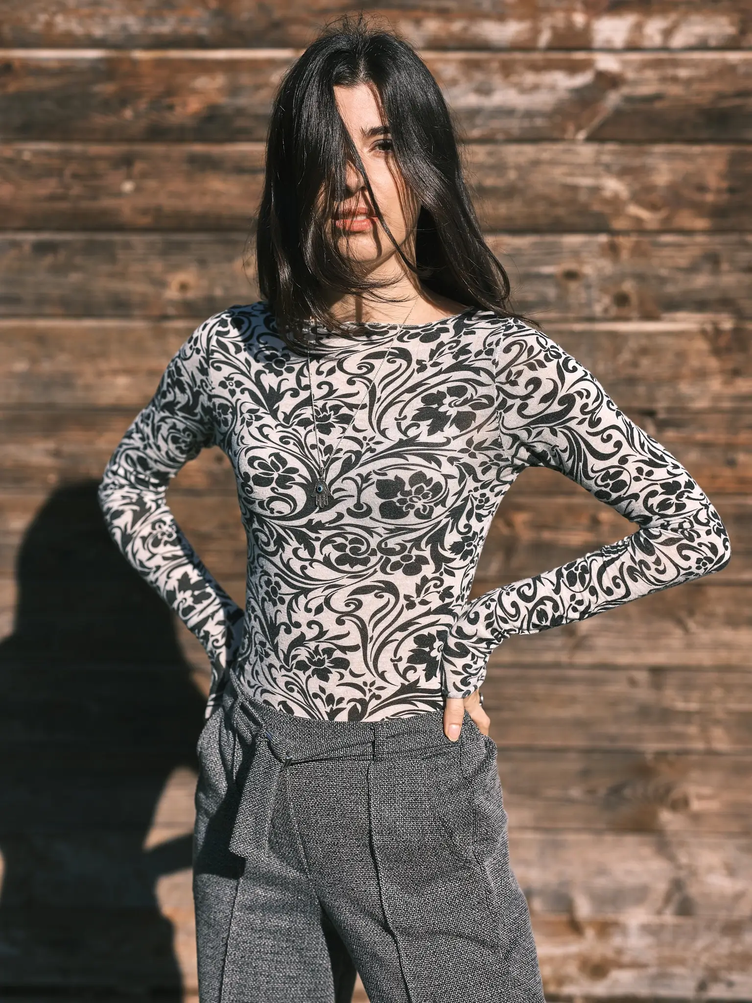Giada standing in front of a wooden wall, hair moved by the wind, natural portrait.