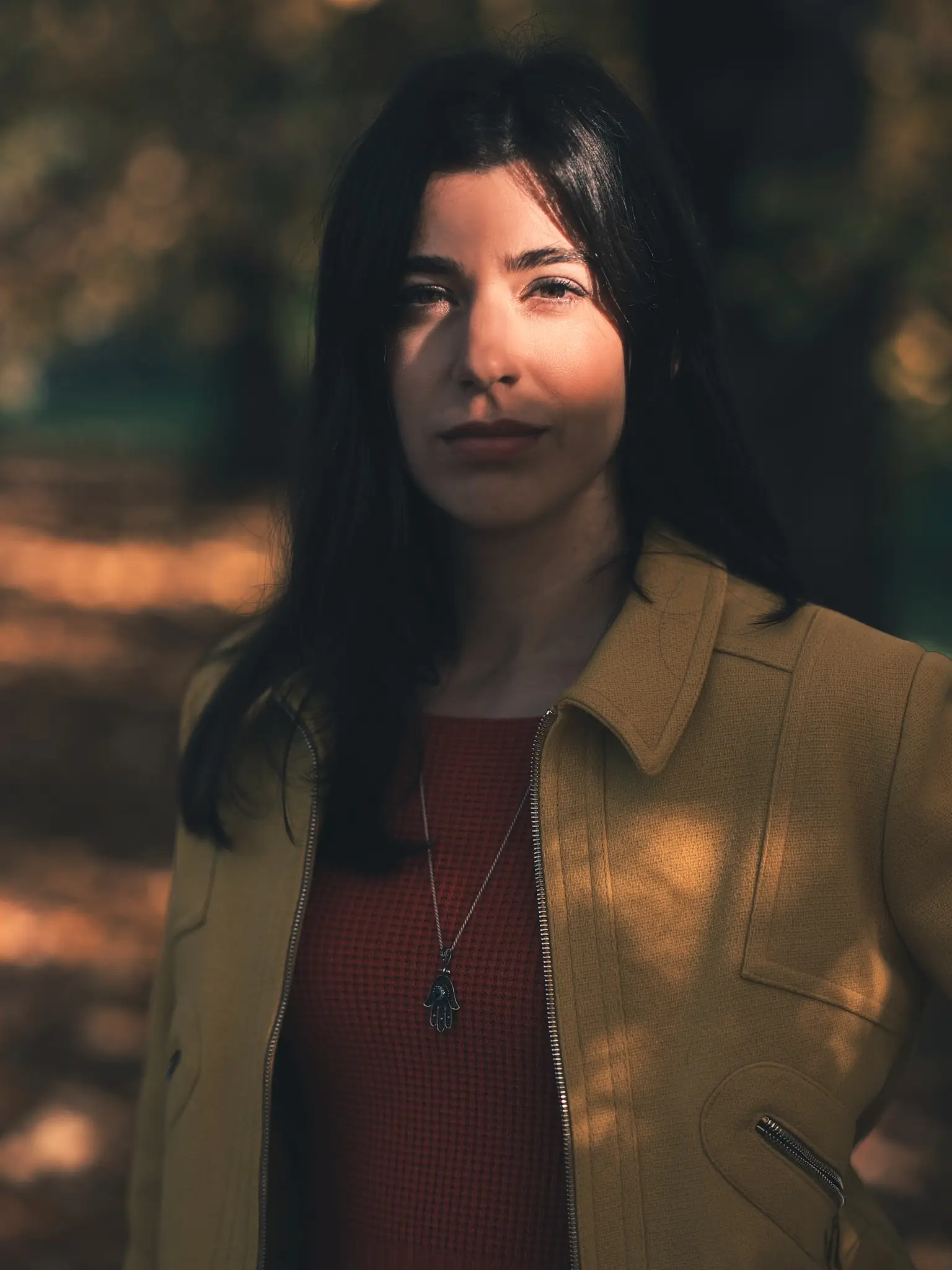 Close-up of Giada in shade, sunlight through trees highlighting her face, yellow jacket and orange top.